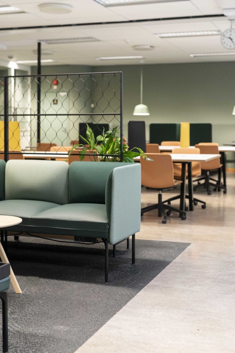 Sofagruppe plassert i åpent landskap. Arbeidsplass rundt langbord bakerst i lokalet. Stoler plassert rundt langbordet. Foto