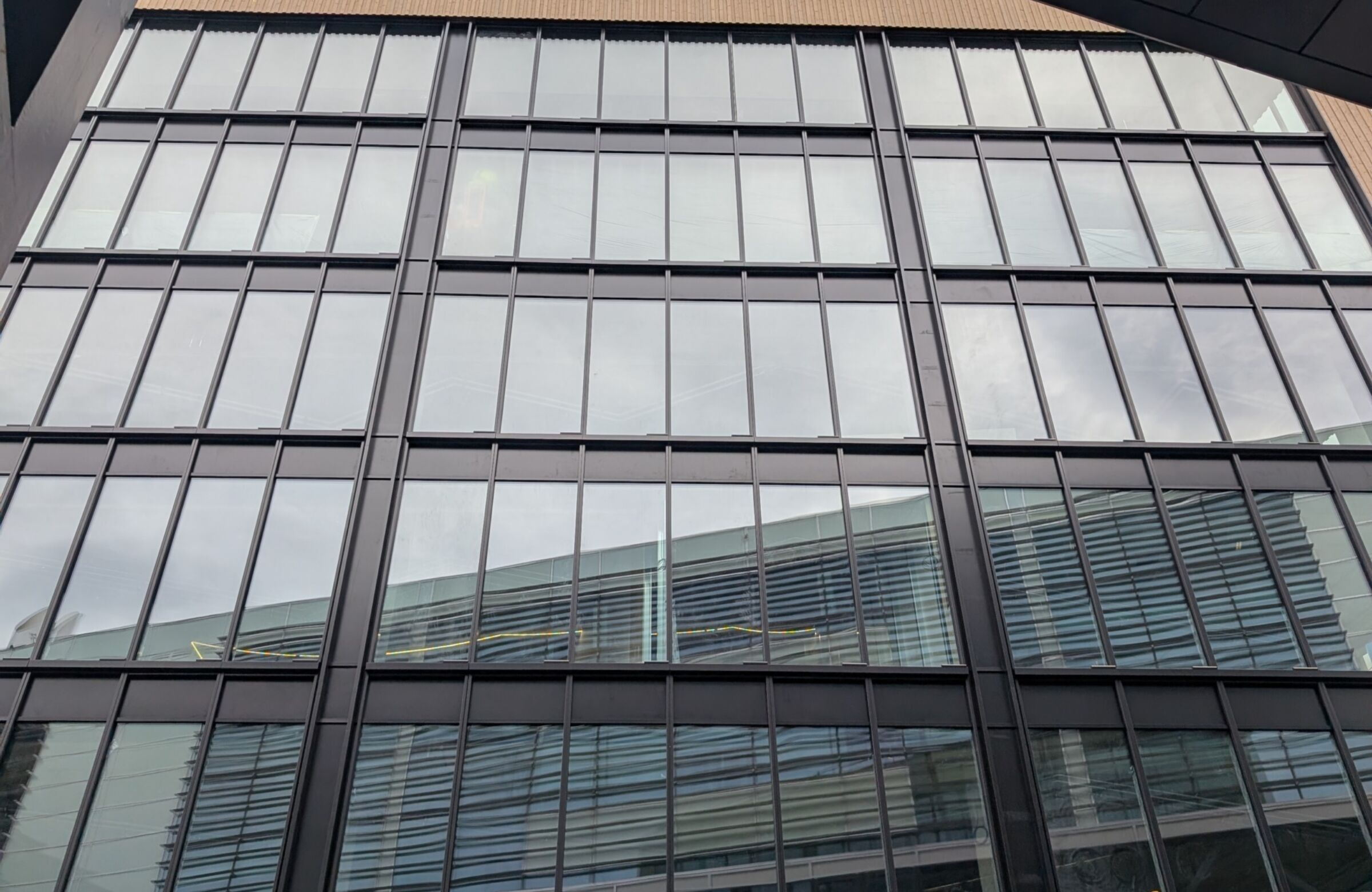 Fasade på moderne kontorbygg med store glassfelt og mørke metallrammer, sett fra bakkenivå med himmel i bakgrunnen. Foto.