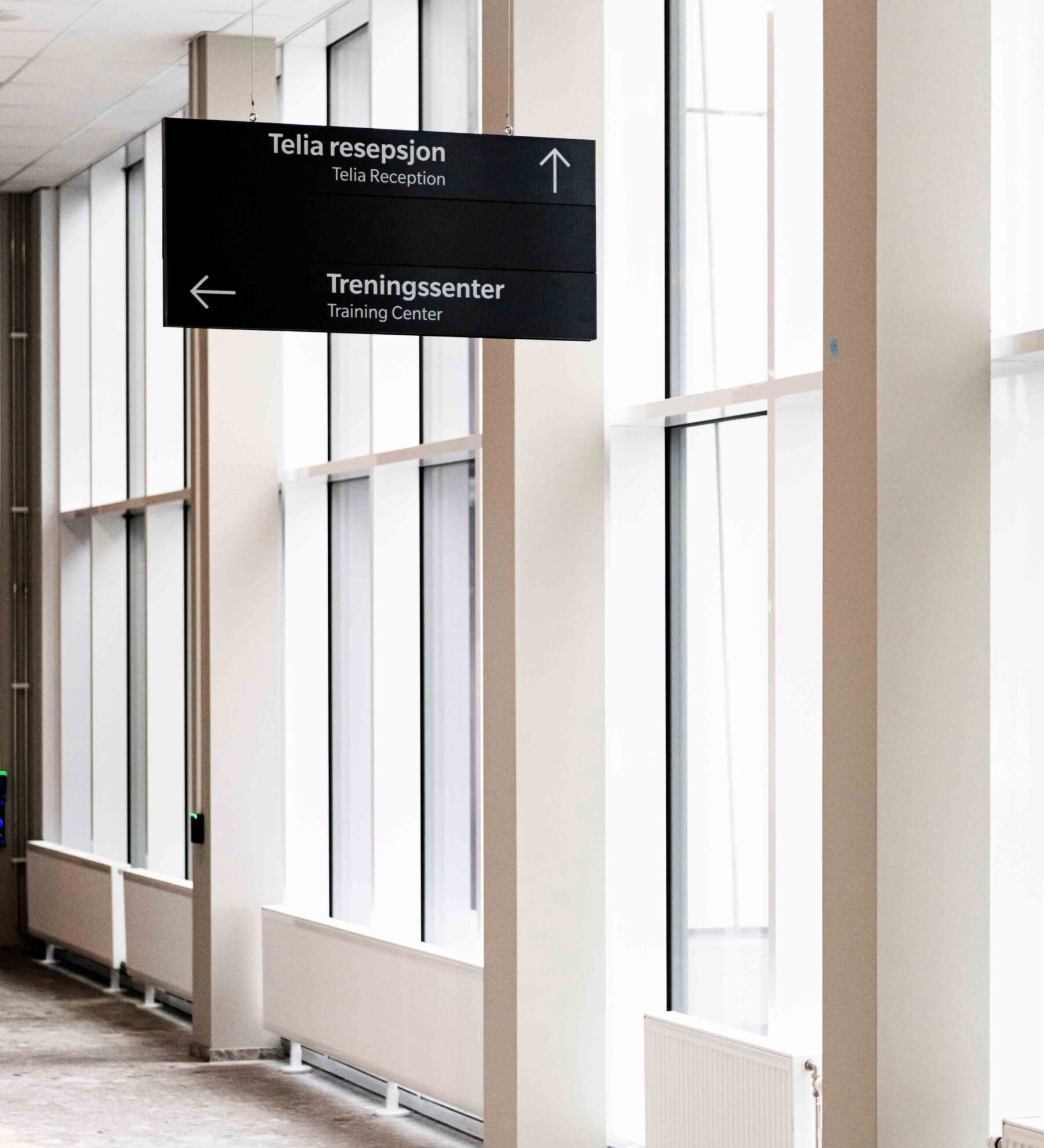 Wayfinding henger fra taket i gangsone. Store vinduer langs fasaden. Foto