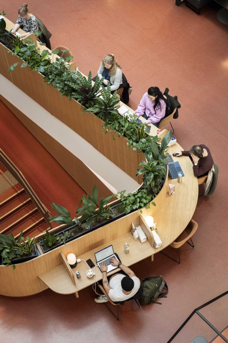 Spesialtilpasset bord montert langs gelender på trappen. Studenter sitter og jobber langs bordet. Foto