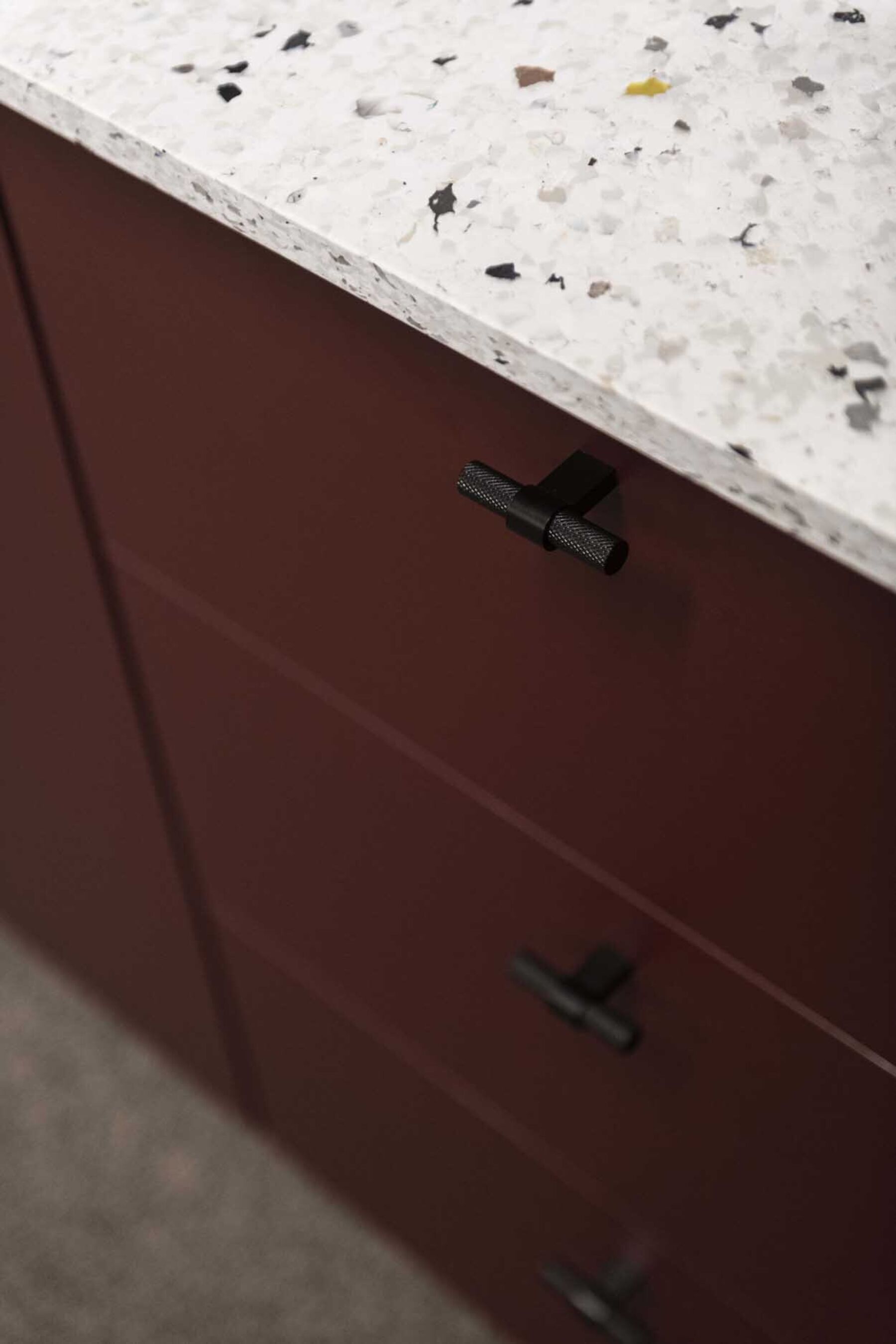 Detaljer av bardisk. Mørkerøde fronter, håndtak i sort metall og benkeplate med tekstur. Foto.