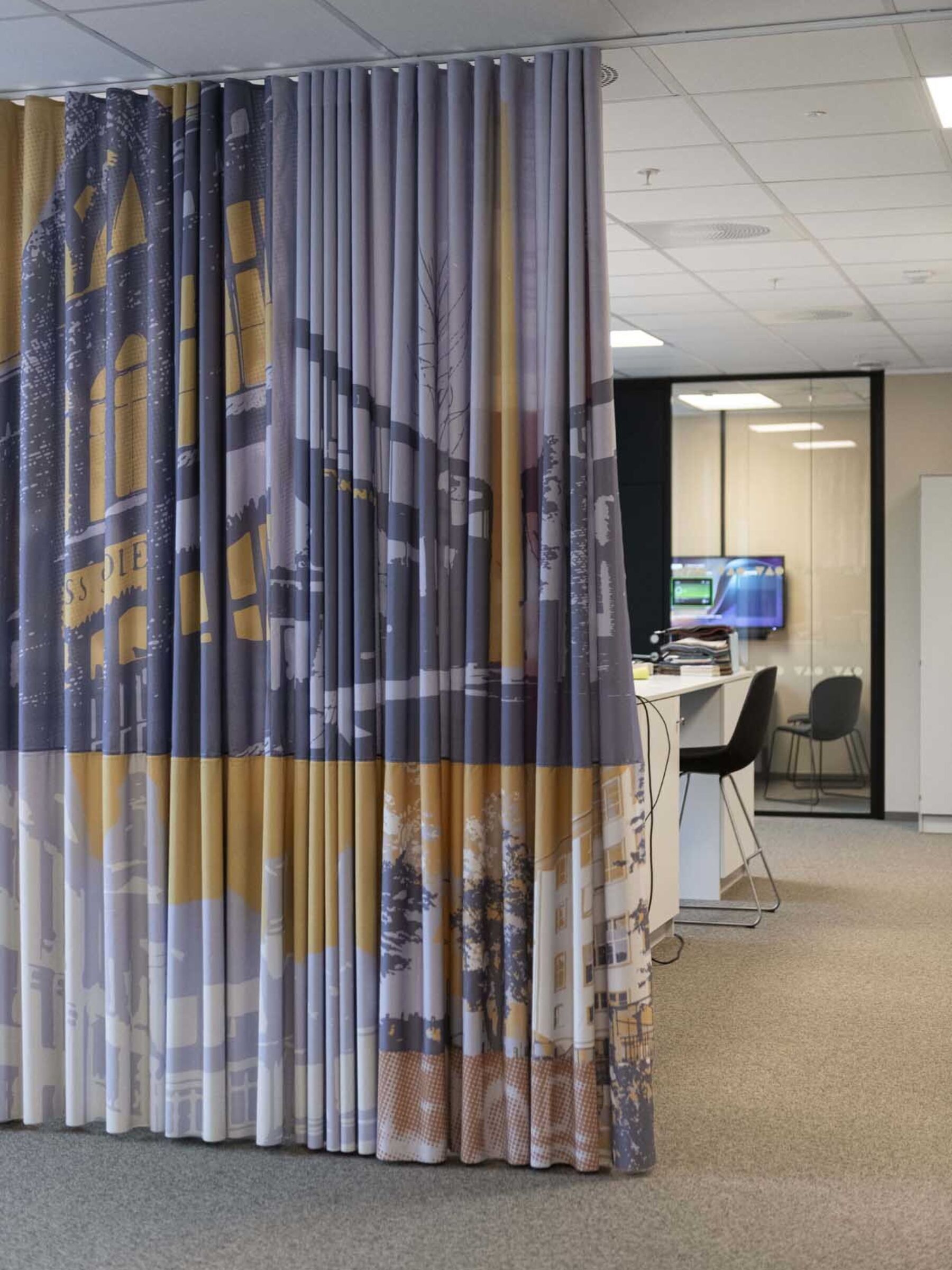 Unik gardin henger fra tak til gulv, arbeidsbord- og stoler i bakgrunnen. Foto.