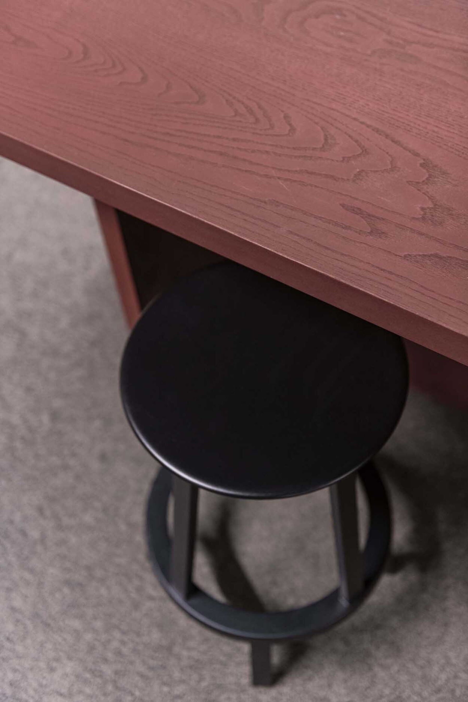 Detaljbilde av et spesialbygd, burgunderfarget bord med en sort krakk. Foto.