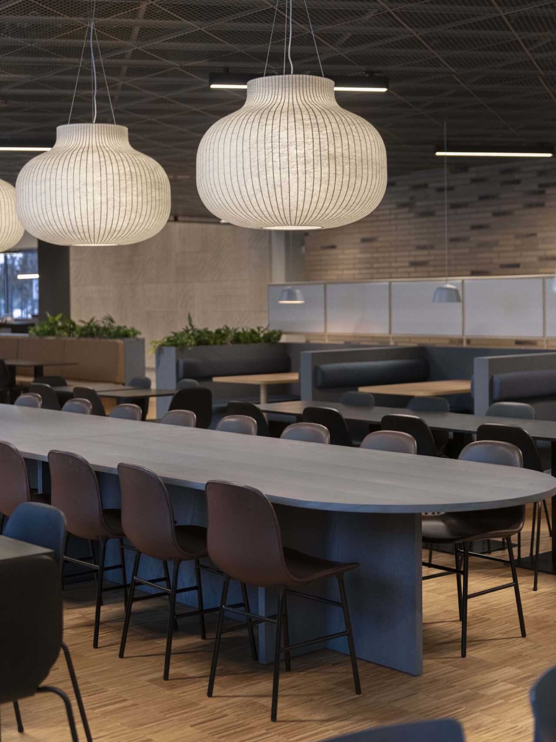 Rader med stoler og bord i kantine. Tre store lamper henger over ett bord. Foto.